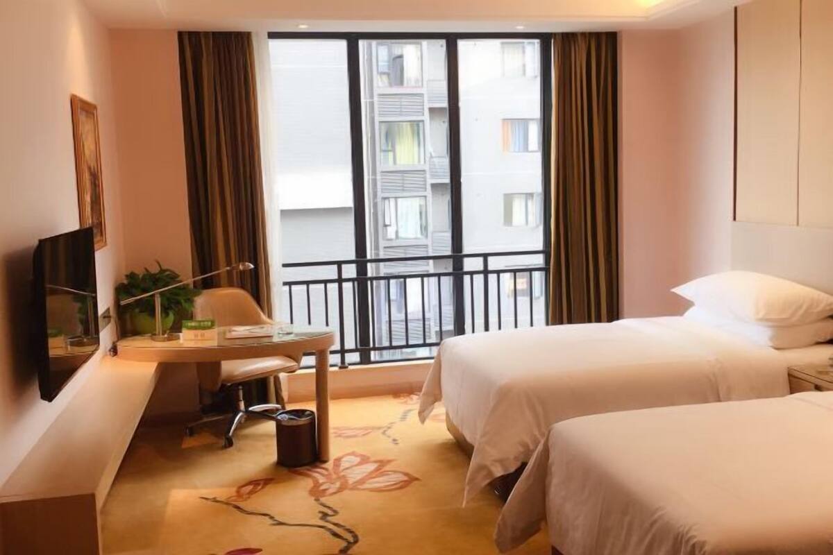 Habitación de hotel con dos camas, un escritorio con silla, televisor y ventana con cortinas.