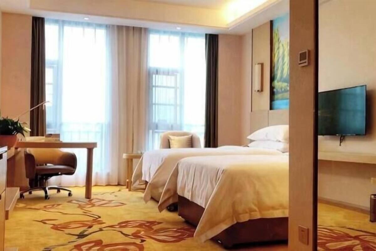 Habitación de hotel con dos camas, un escritorio, una silla, un televisor y un ventanal con cortinas.