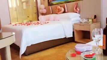 A hotel room with a bed, a bedside table with a glass of wine, and a small table with a glass of water and a fruit.