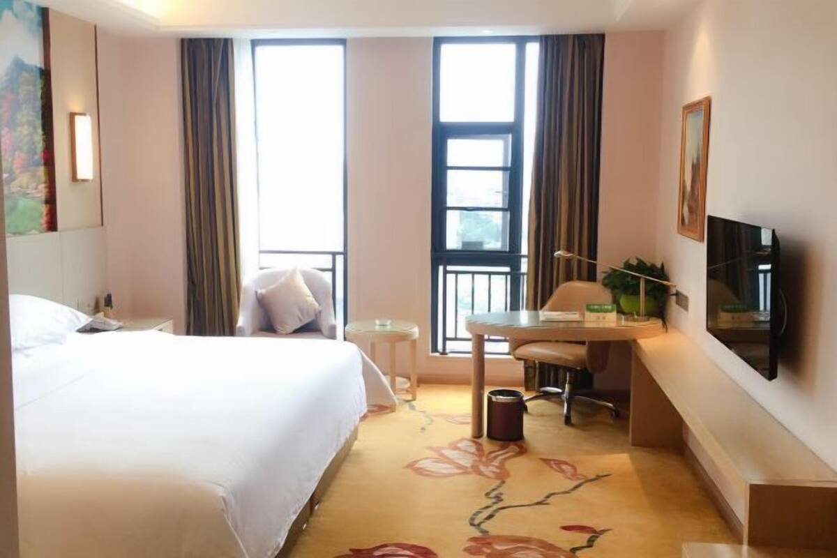 Una habitación de hotel con cama, escritorio y silla, televisor y ventana con cortinas.