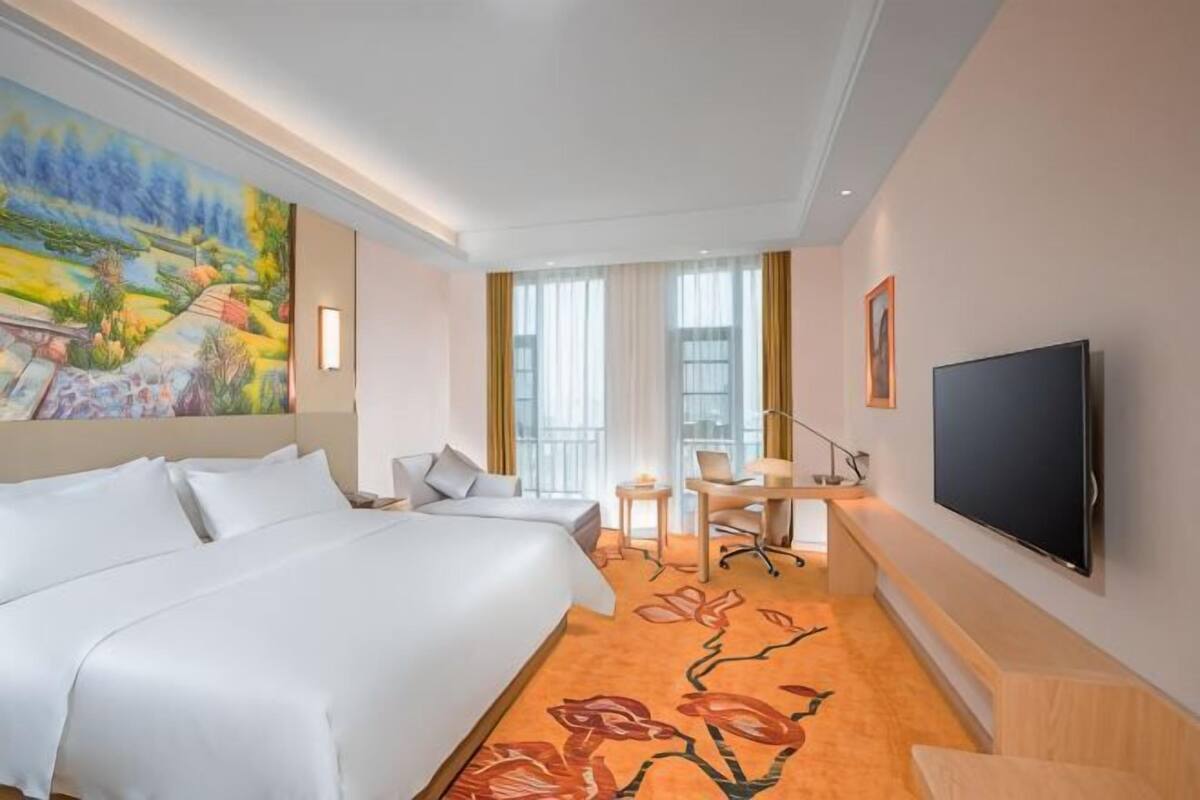 Una habitación de hotel con una cama grande, un escritorio, una silla, un televisor y un cuadro en la pared.