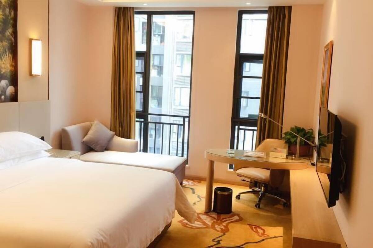 Habitación de hotel con dos camas, un escritorio, una silla, un televisor y una ventana con cortinas.