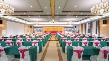 A banquet hall with rows of tables, each with a green tablecloth and pink sashes, and a stage at the front.