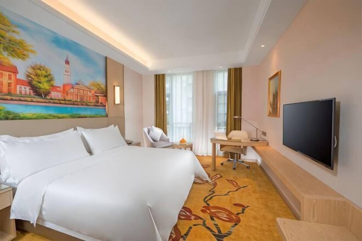 Habitación de hotel con cama, escritorio, silla, televisor y un cuadro en la pared.