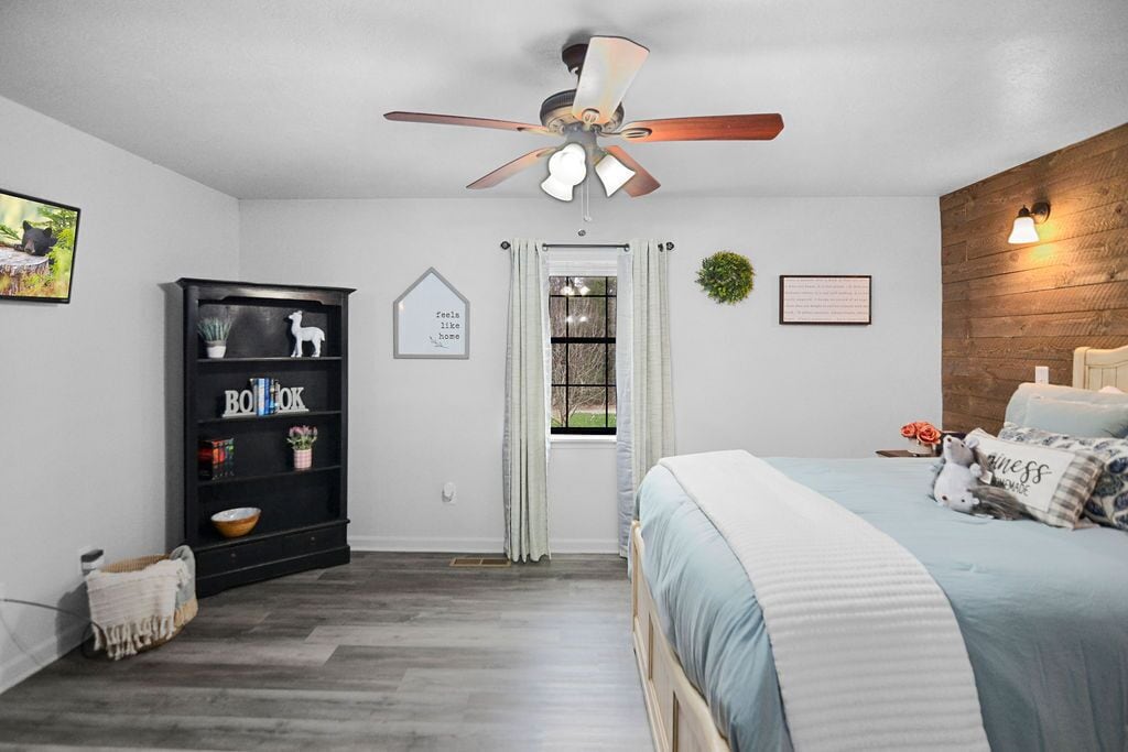 A bedroom with a bed, a ceiling fan, a black bookshelf, and a window with curtains.