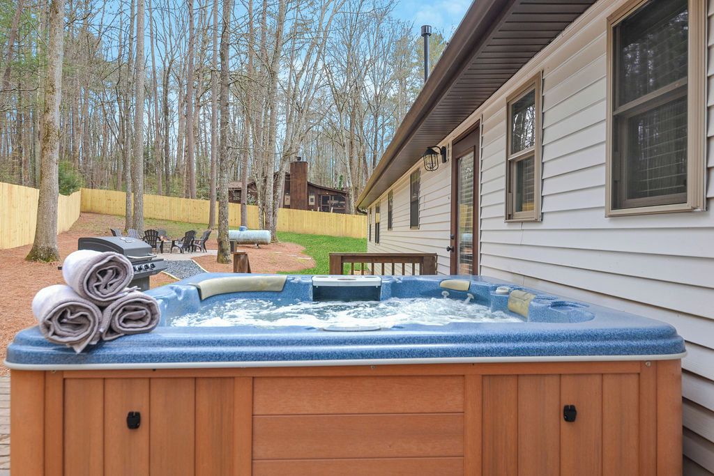 A hot tub in a backyard with a wooden deck, a barbecue grill, and a wooden fence.