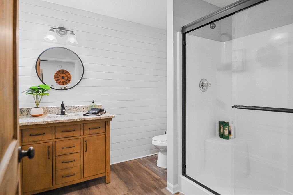 Un baño moderno con tocador de madera, espejo redondo y cabina de ducha con mampara de vidrio.