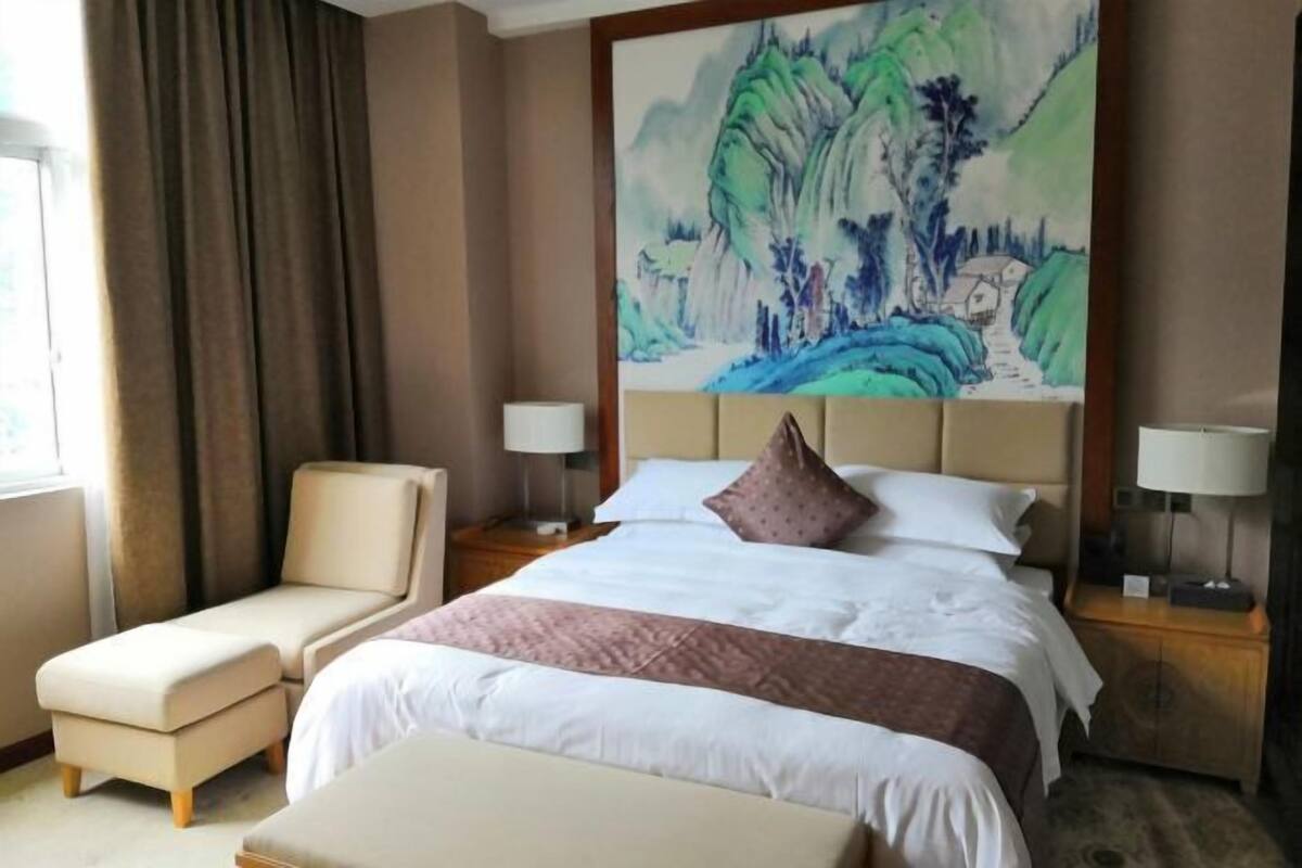 Een hotelkamer met een groot bed, een stoel, een nachtkastje en een schilderij aan de muur.