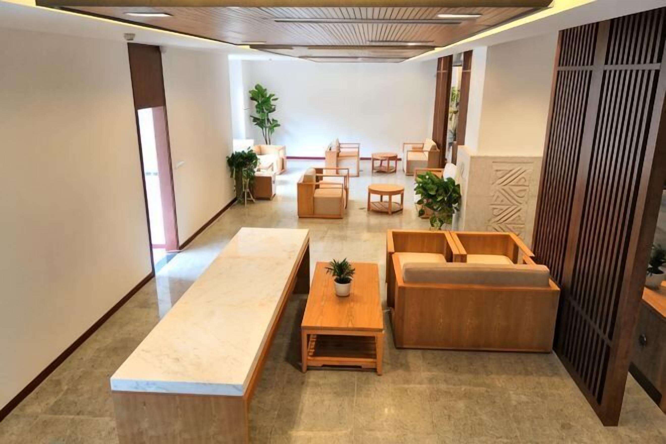 A hotel lobby with a long reception desk, seating area with sofas and chairs, and a decorative wall with vertical elements.