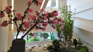 A modern indoor space with a large artificial pink flowering plant in a vase, a bamboo plant, and a rock garden.