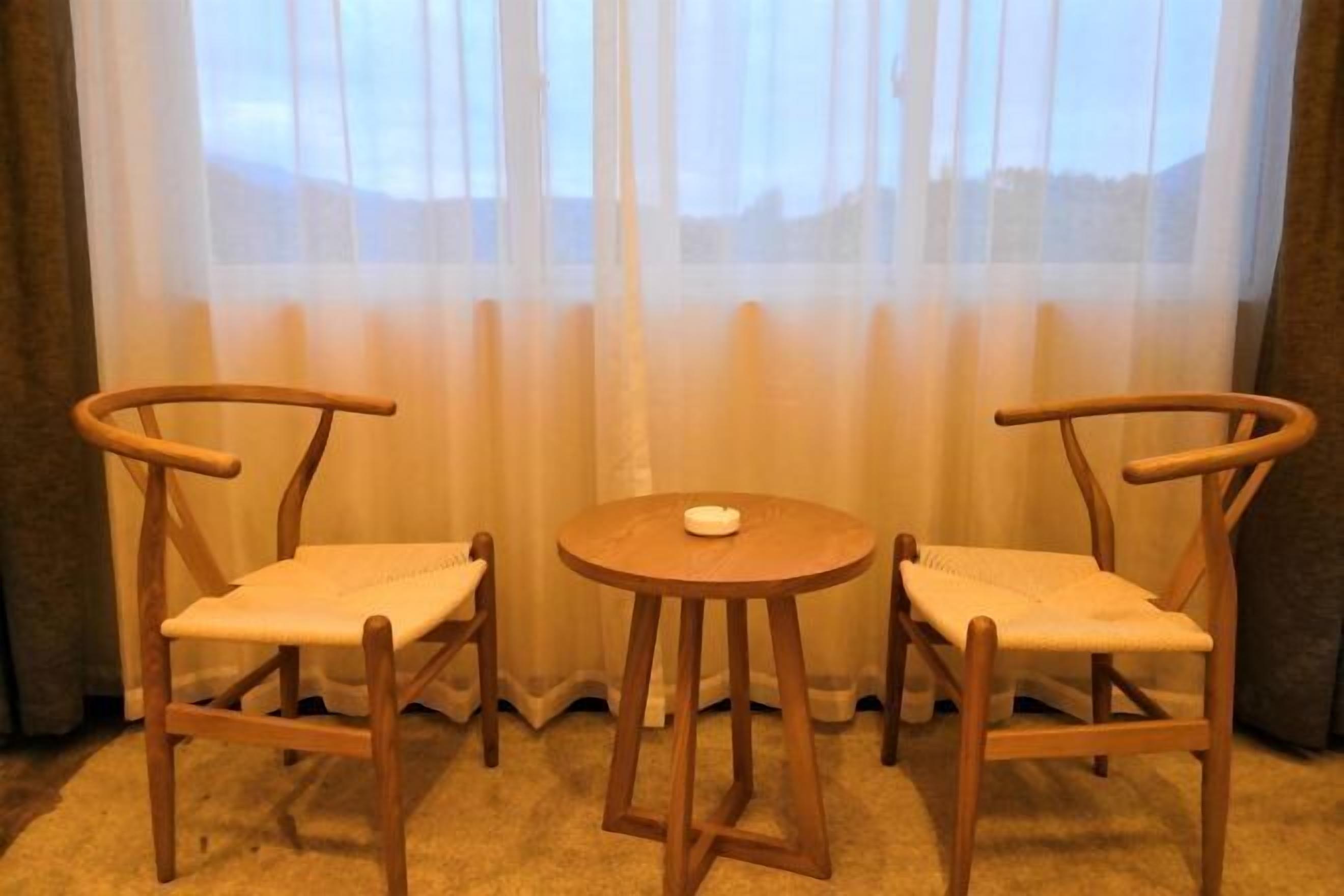 Two wooden chairs with cushioned seats and a small round table in front of a window with sheer curtains.