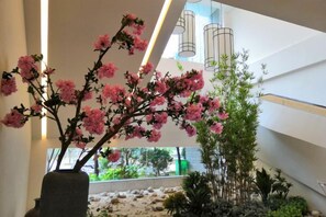 A modern indoor space with a large potted plant with pink flowers, a bamboo structure, and a stone wall. - Pristime International Holiday Hotel (Yinjiang)