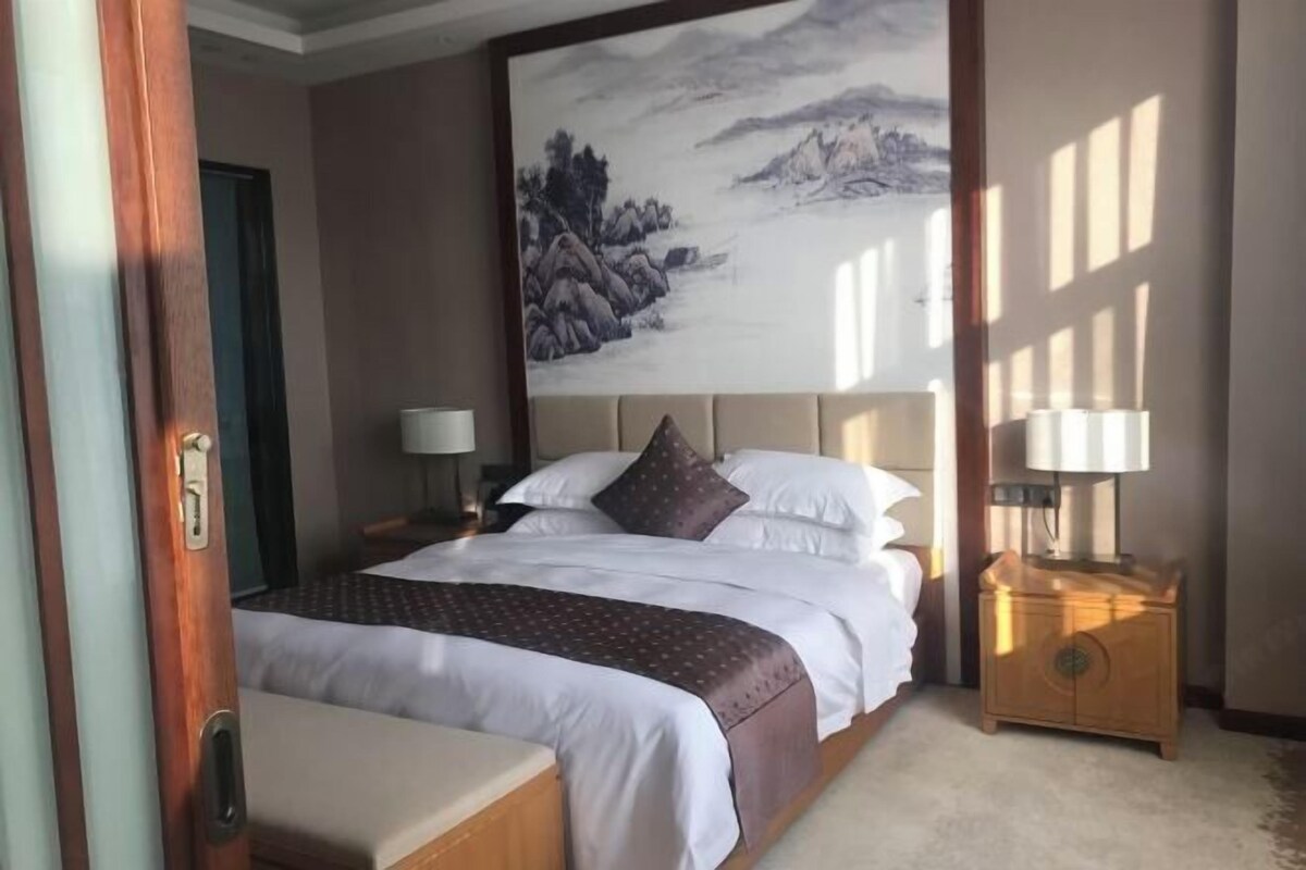 A hotel room with a bed, bedside tables, and a large painting on the wall.