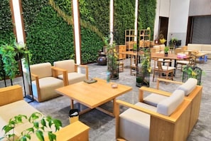 A modern lounge area with wooden furniture, green wall decor, and a variety of seating options. - Pristime International Holiday Hotel (Yinjiang)