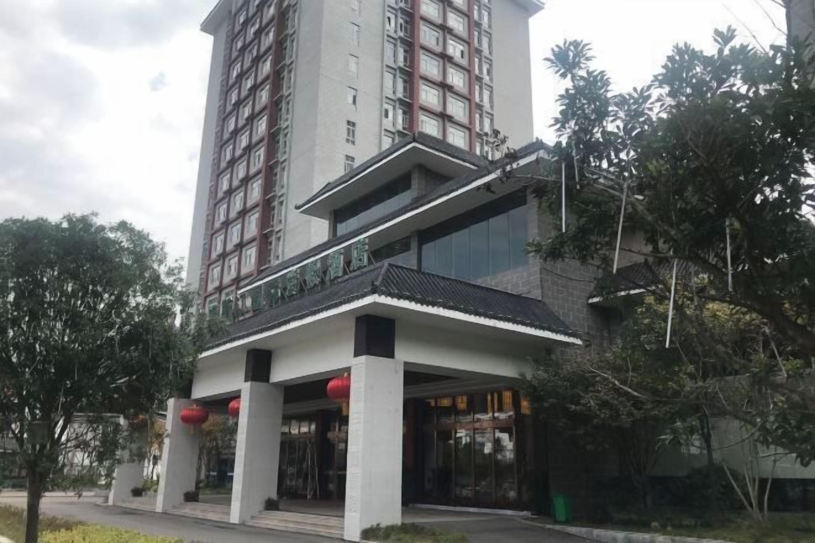 Un hôtel à plusieurs étages au design moderne, doté d’une entrée imposante avec une allée couverte et des lanternes rouges.