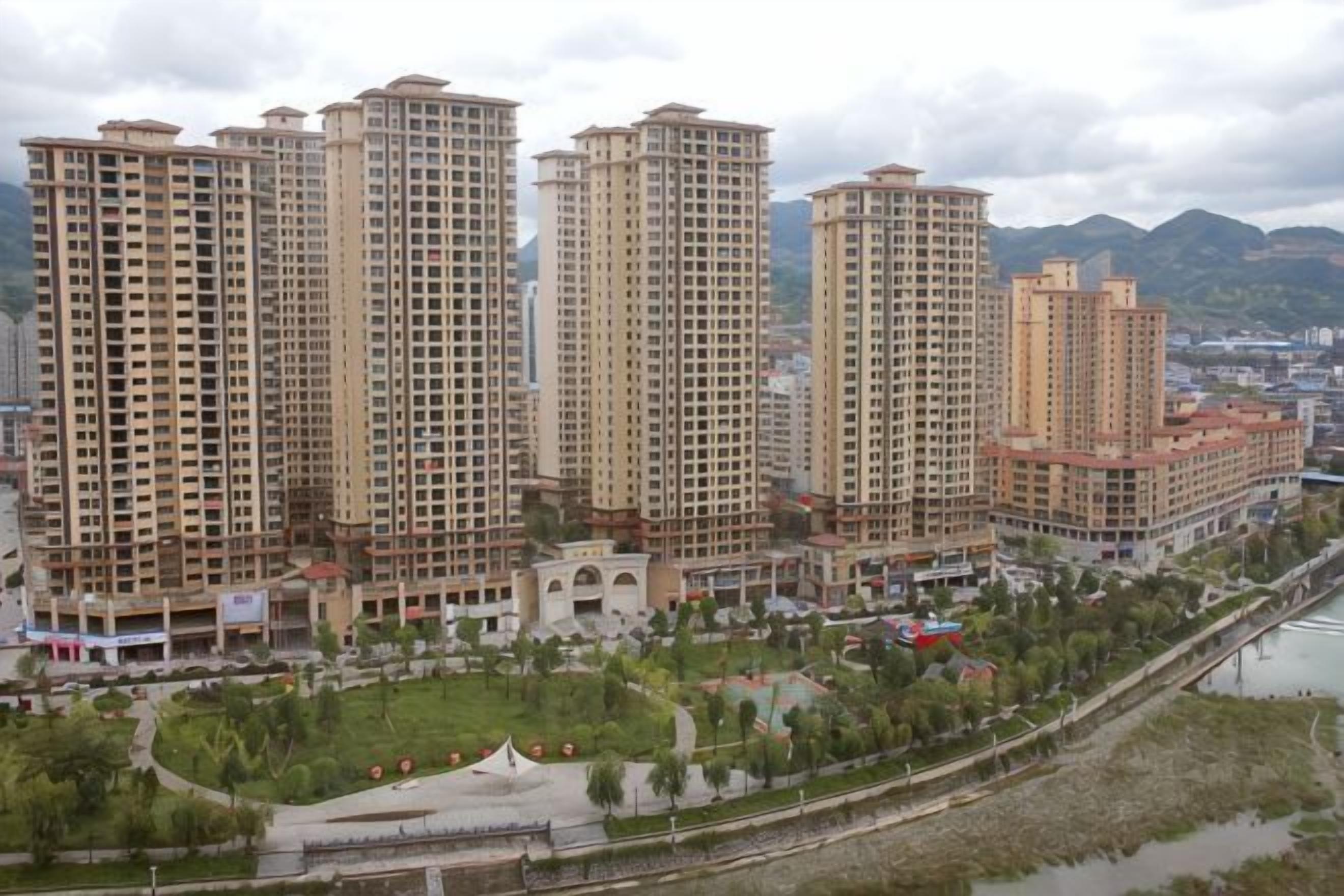 Un complejo de viviendas de gran altura con varios edificios de apartamentos, un río y un puente al fondo.
