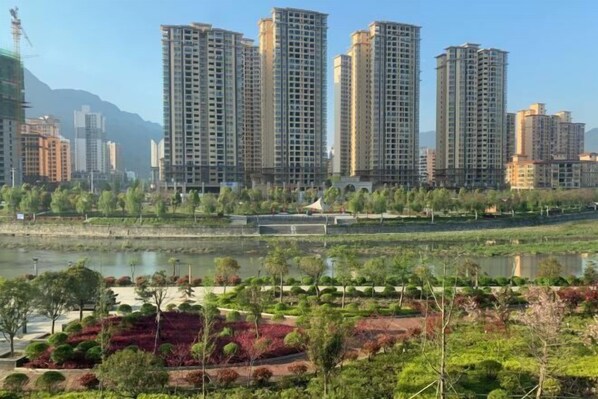 A high-rise residential building complex with multiple apartment towers, a river in the foreground, and landscaped areas with trees and shrubs. - Pristime International Holiday Hotel (Yinjiang)