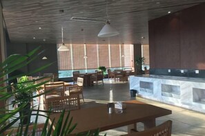 A spacious indoor area with wooden tables and chairs, a large window, and a stone counter. - Pristime International Holiday Hotel (Yinjiang)