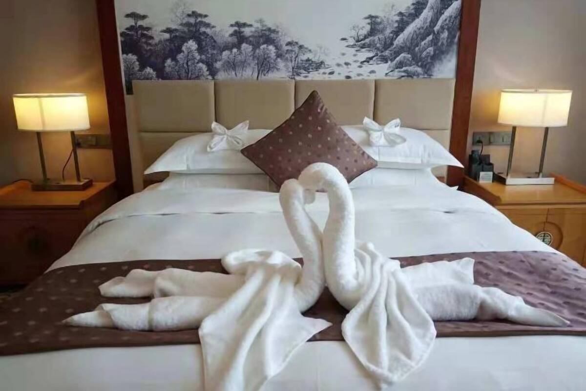 Hotelkamer met een bed, twee nachtkastjes met lampen, een hoofdbord met een schilderij, en een deken met handdoeken gerangschikt in de vorm van zwanen.