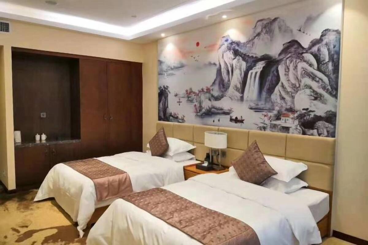 Een hotelkamer met twee bedden, een grote muurschildering, een garderobe en een nachtkastje met een lamp.