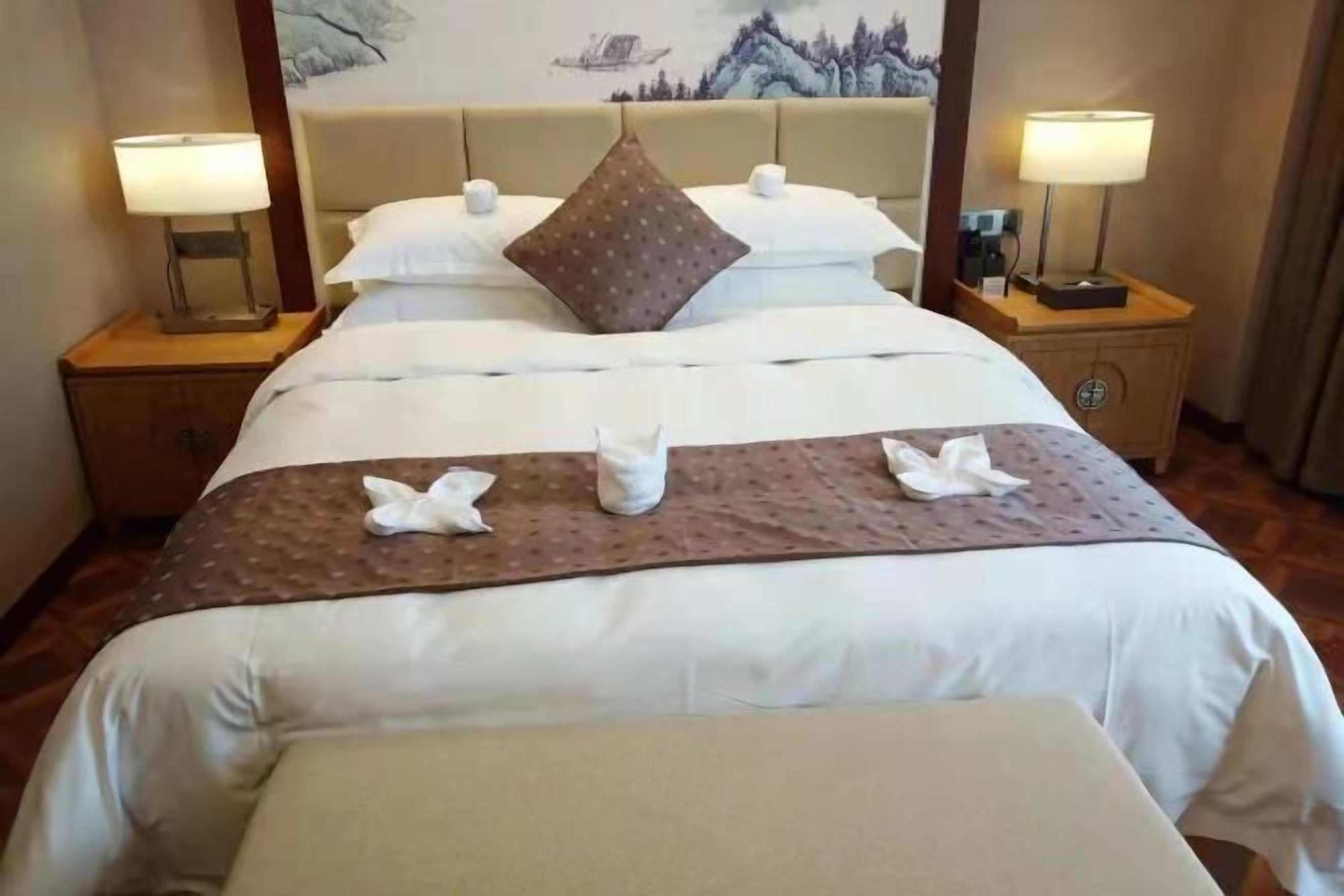 Ein Hotelzimmer mit einem großen Bett, zwei Nachttischen, einem Kunstwerk-verzierten Kopfteil und einem kleinen Tisch mit einer Lampe.