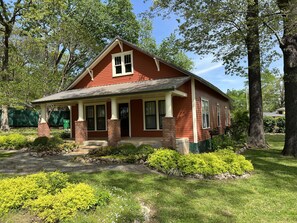 Classic single-story house with a gable roof and front porch, set amidst well-maintained lawns and shrubs.