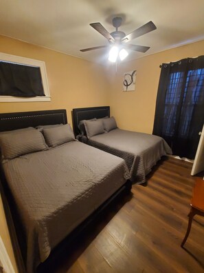 Quarto com duas camas, ventilador de teto e janela com cortinas.