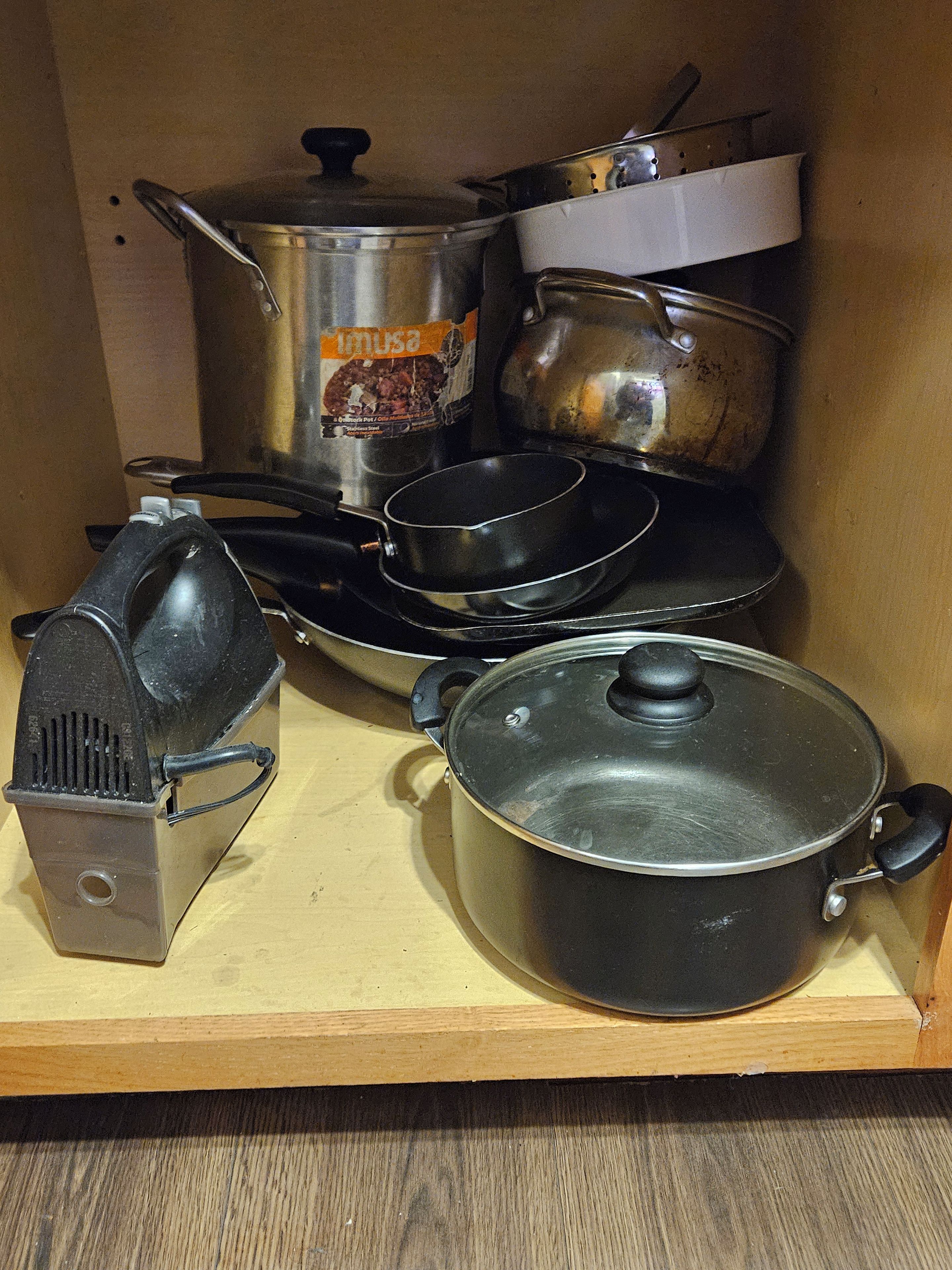 Una cocina con estufa, ollas, un rallador y una sartén.
