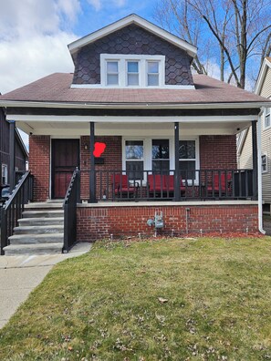 A two-story house with a brick facade, a front porch with a railing, and a red heart decoration on the wall. - Spacious 4 bedrooms, 6 beds, 2 baths (Detroit)