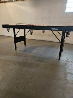A billiards table with a net, positioned in a room with a concrete floor and a white wall. - Spacious 4 bedrooms, 6 beds, 2 baths (Detroit)