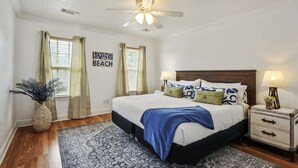 Un dormitorio con cama, mesitas de noche, ventilador de techo, ventana con cortinas y un cartel en la pared.