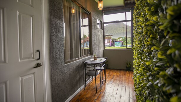 A room with a wooden floor, a small table with two chairs, a potted plant, and a view of a mountain through a window. - Coati Arenal Lodge (La Fortuna)