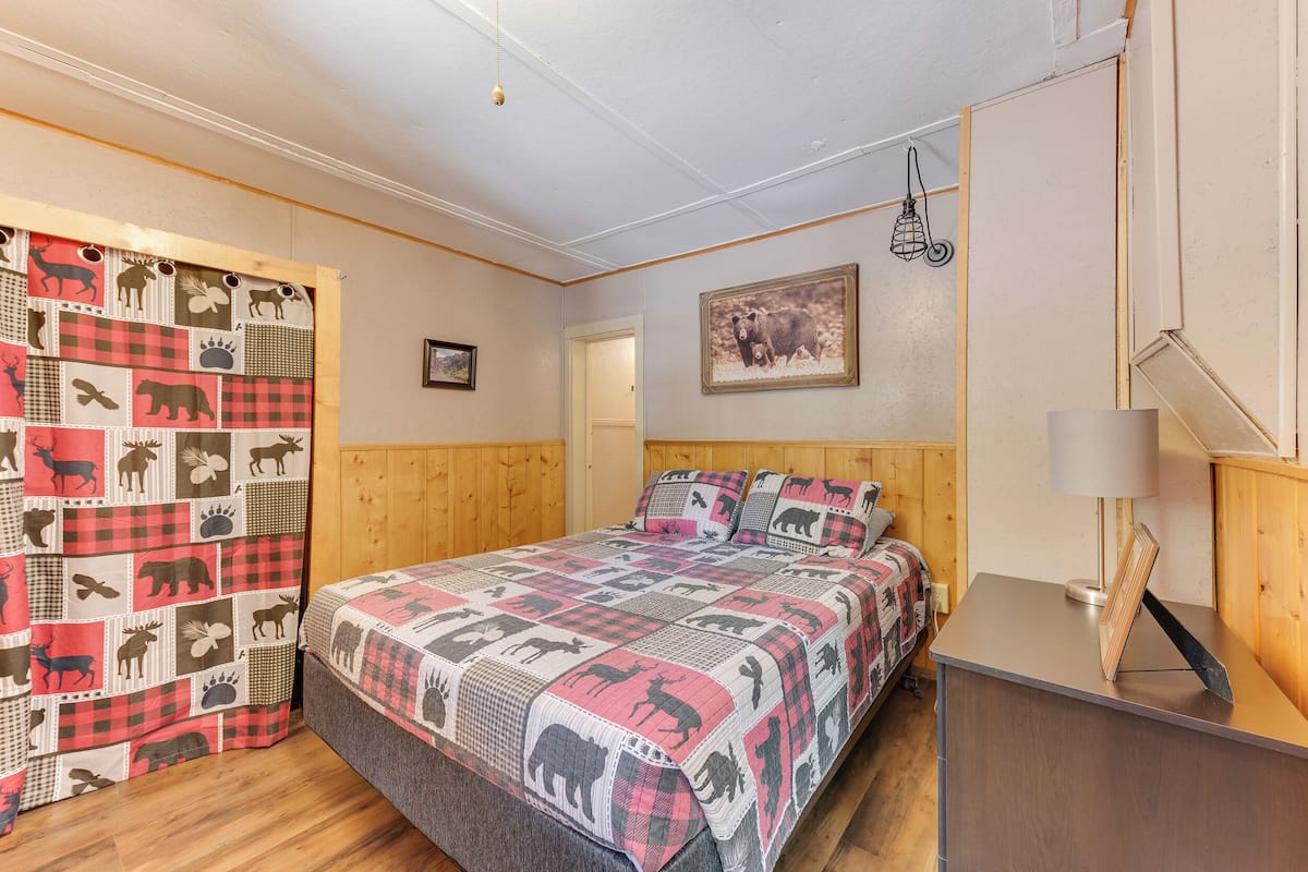 Ein Schlafzimmer mit Bett, Holz-Kopfteil, Nachttisch mit Lampe, einer Decke mit Tiermustern und einem Wandbild in einem Rahmen.