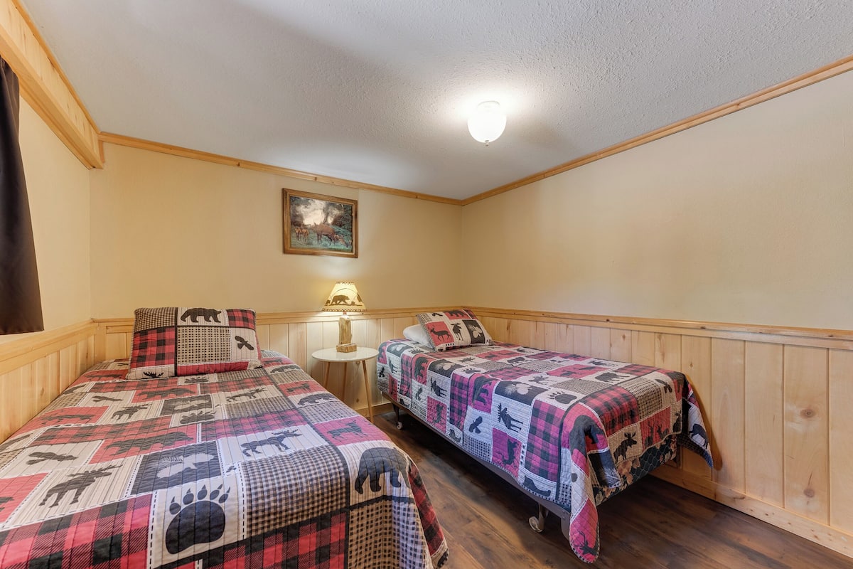 Ein Zimmer mit zwei Betten, jedes mit einer gesteppten Decke mit Tiermotiven. Es gibt einen kleinen runden Tisch mit einer Lampe und ein Bild an der Wand.