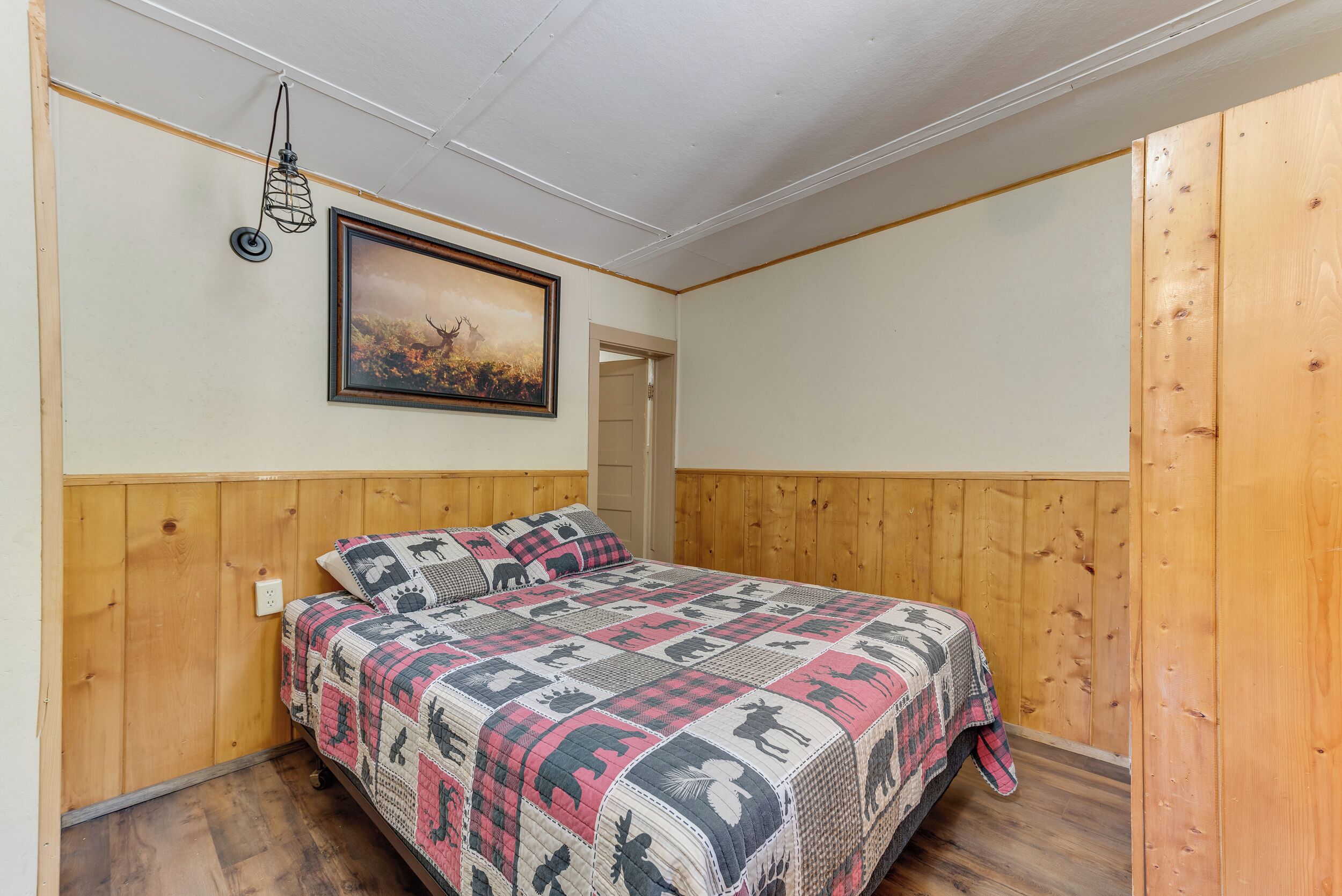Una camera da letto con testiera in legno, copripiumino trapuntato, un quadro appeso al muro e un lampadario.