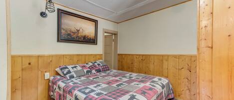 Una camera da letto con testiera in legno, copripiumino trapuntato, un quadro appeso al muro e un lampadario.