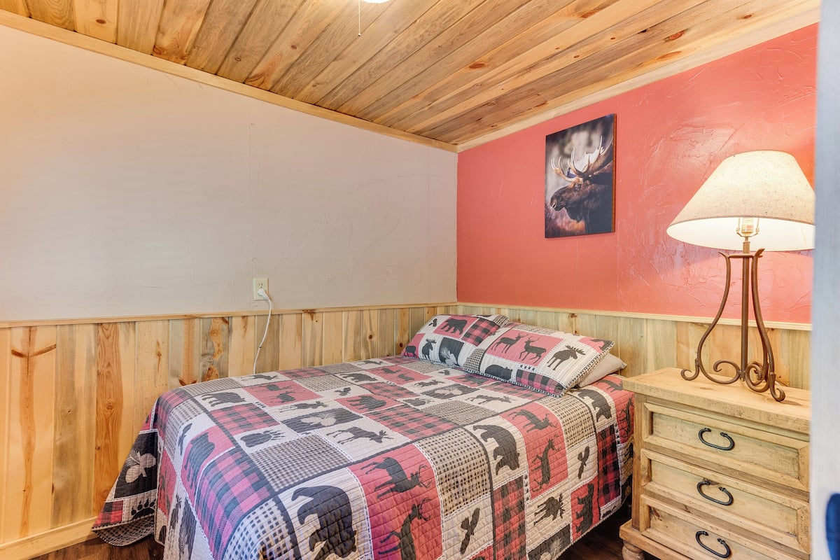Ein Schlafzimmer mit Holzboden, einem Bett mit geblümter Bettdecke, einer Kommode mit Lampe und einem Wandbild.