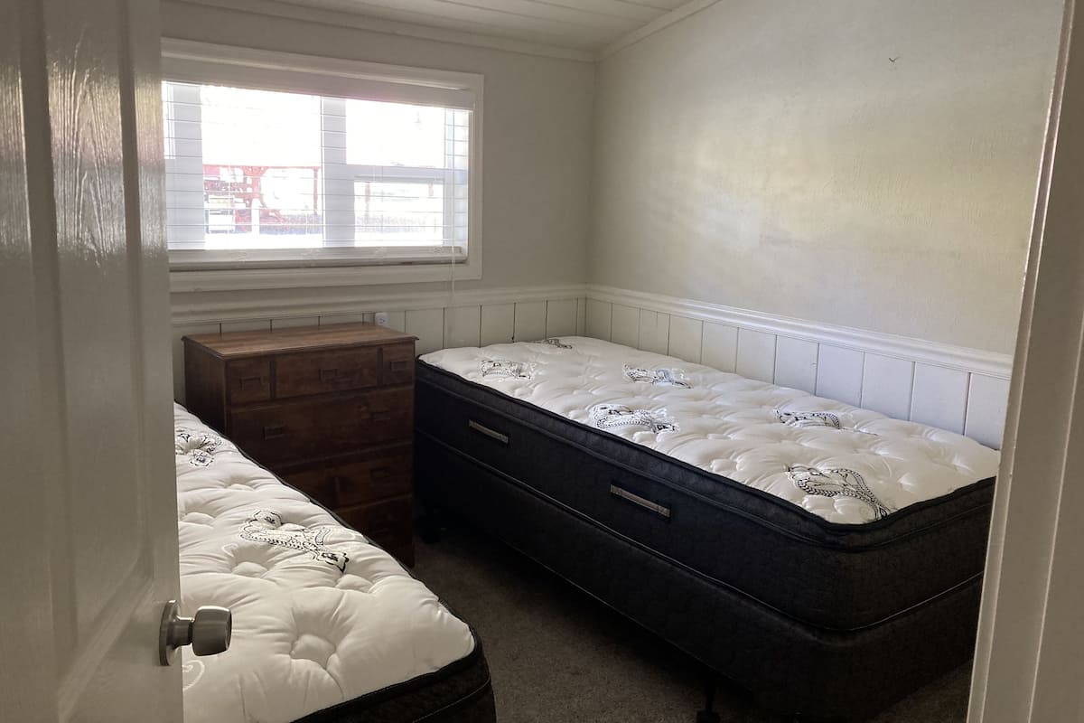 Ein Schlafzimmer mit zwei Einzelbetten, einer hölzernen Kommode und einem Fenster mit Jalousien.
