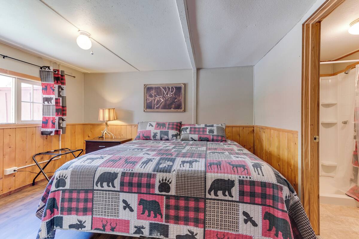 Ein Schlafzimmer mit einem großen Bett, Holzwänden, einem Fenster mit Blick, einer Lampe und einem an der Wand befestigten Kunstwerk.