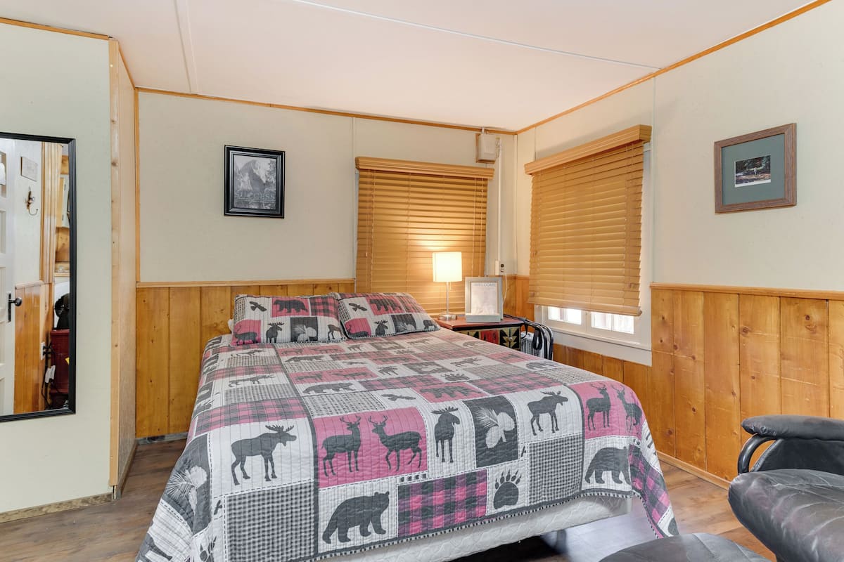 Ein Schlafzimmer mit einem großen Bett, Holzwänden, einer Holztür und einem Fenster mit Jalousien.