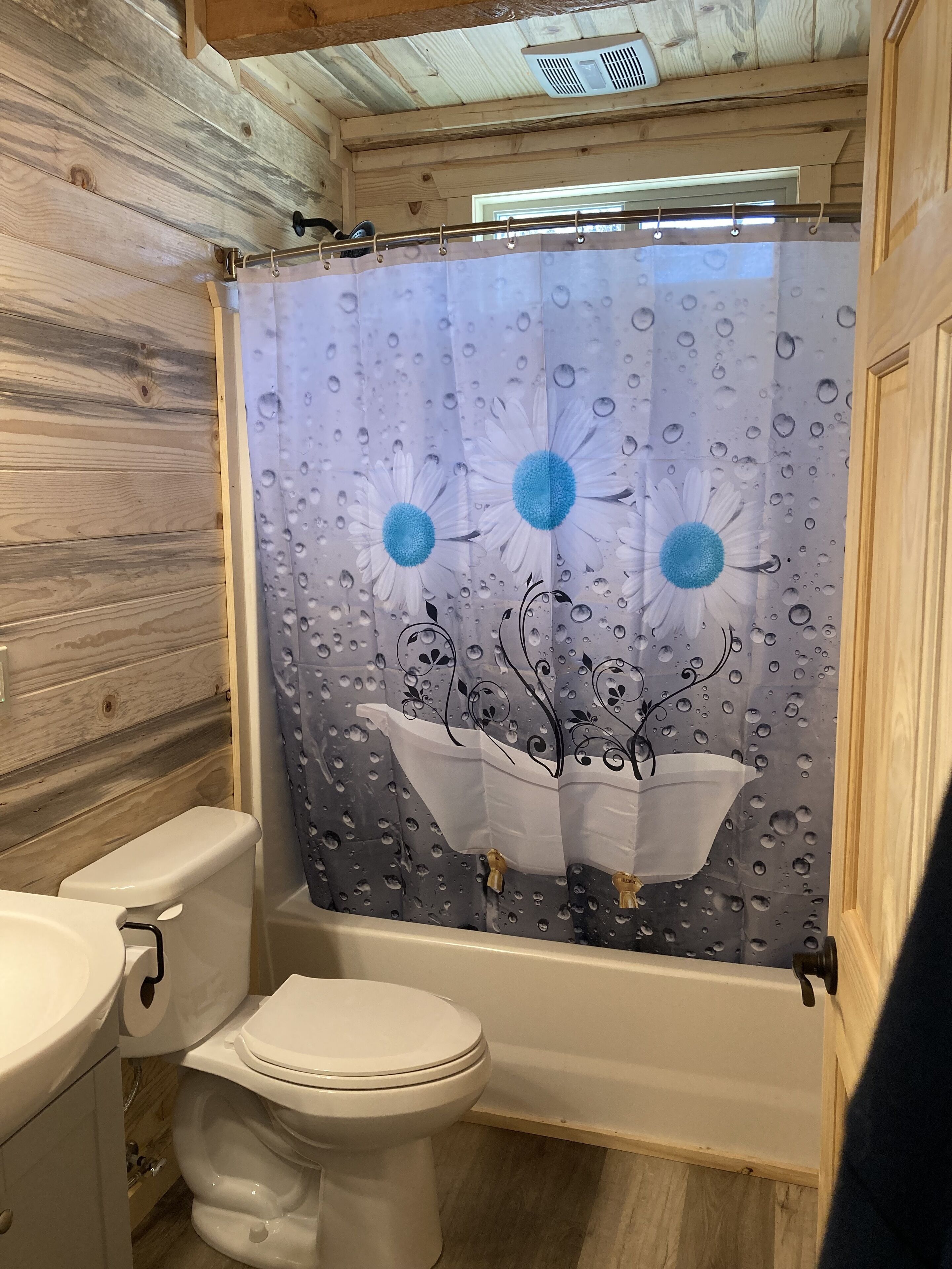 A bathroom with a toilet, a shower curtain with a floral design, and wooden walls.