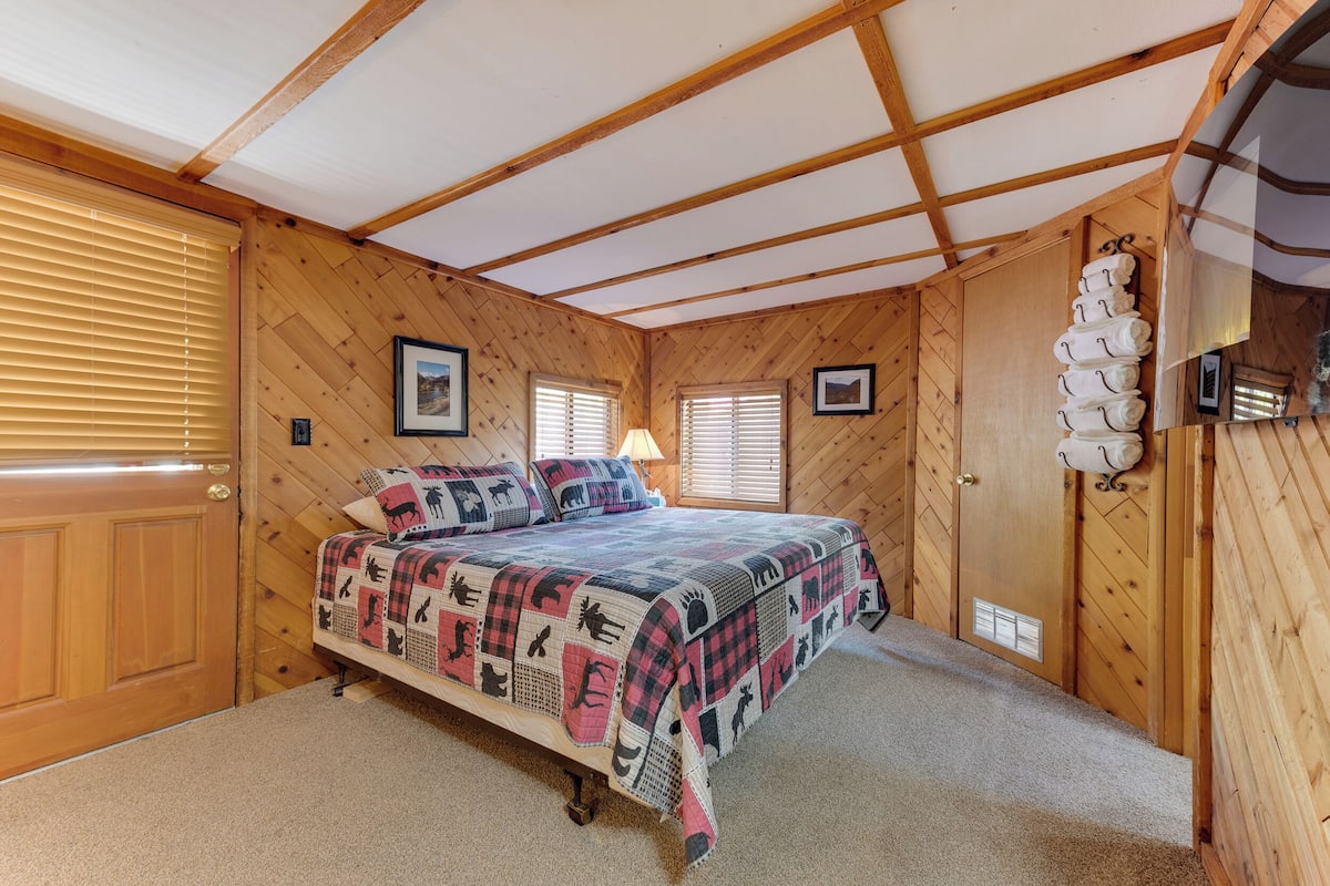 Ein Schlafzimmer mit Holzvertäfelung, einem Bett, zwei Fenstern, einer Tür und einem an der Wand befestigten Handtuchhalter.