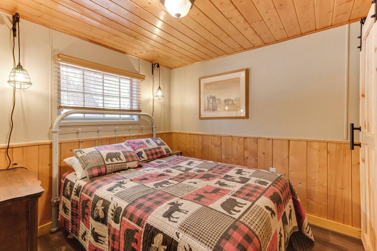 Ein Schlafzimmer mit Holzboden, einem Bett mit einer Decke, einem Fenster mit Jalousien und einem gerahmten Bild an der Wand.