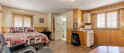 A cozy room with a bed, a desk, a chair, and a kitchenette.