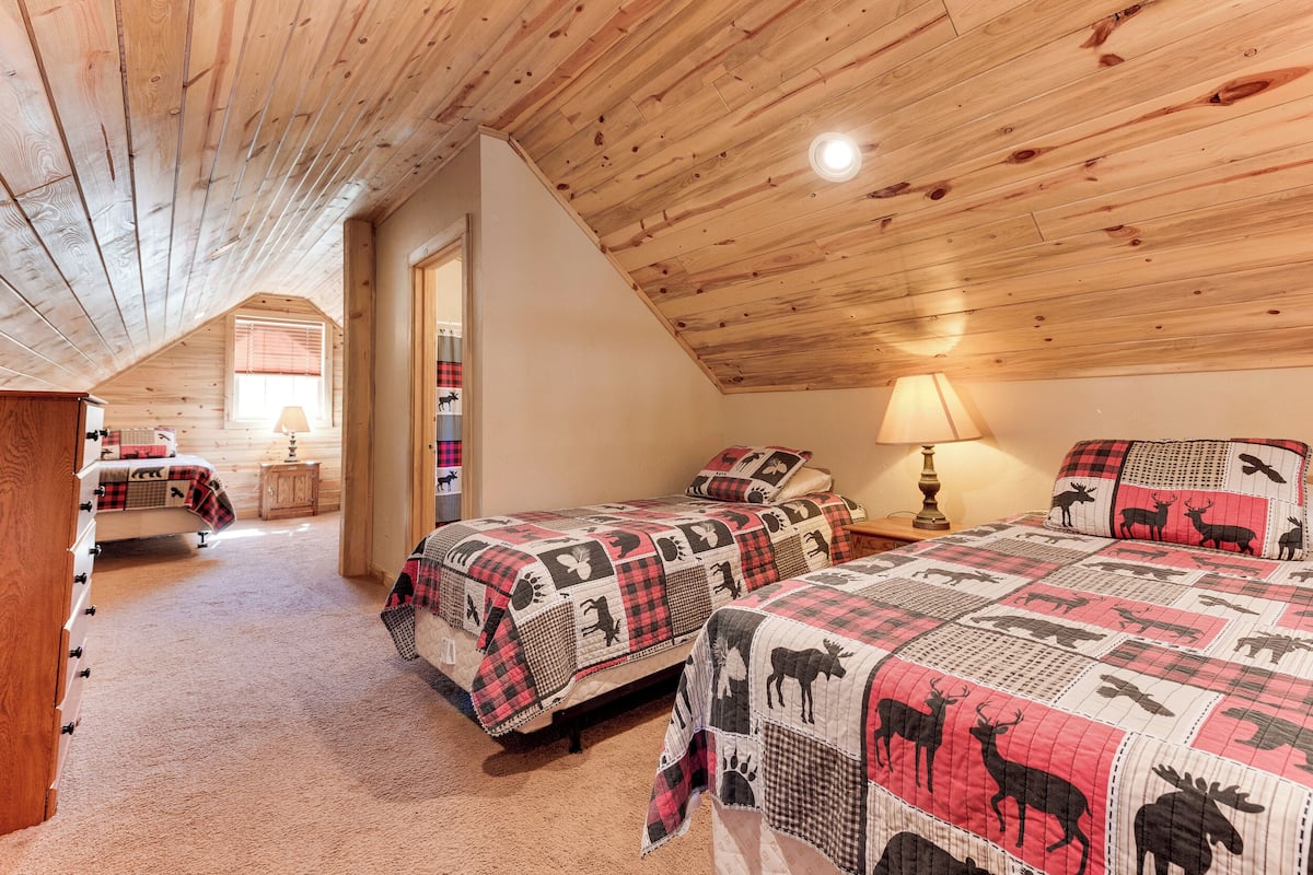 Ein gemütliches Schlafzimmer im Dachgeschoss mit zwei Betten, Holzbalkendecke und geneigter Decke.