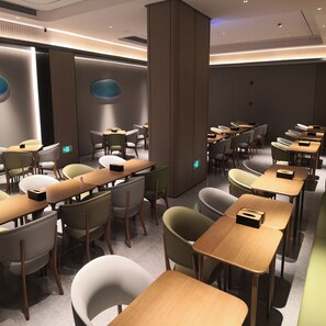 Un salón de conferencias moderno con varias mesas y sillas, equipado con iluminación integrada y un pilar central.