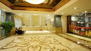 A hotel lobby with a reception desk, a large chandelier, and a patterned floor.