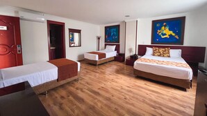 Habitación de hotel con dos camas individuales, una cama doble, suelo de madera, una puerta roja y un cuadro en la pared.