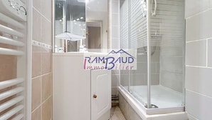A bathroom with a glass shower enclosure, a white vanity with a mirror, and a towel rack.