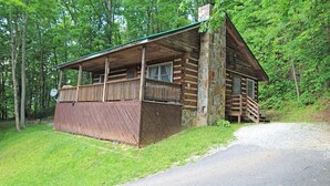A log cabin with a porch, stone chimney, and a gravel driveway. - True Log Cabin (Bryson City)
